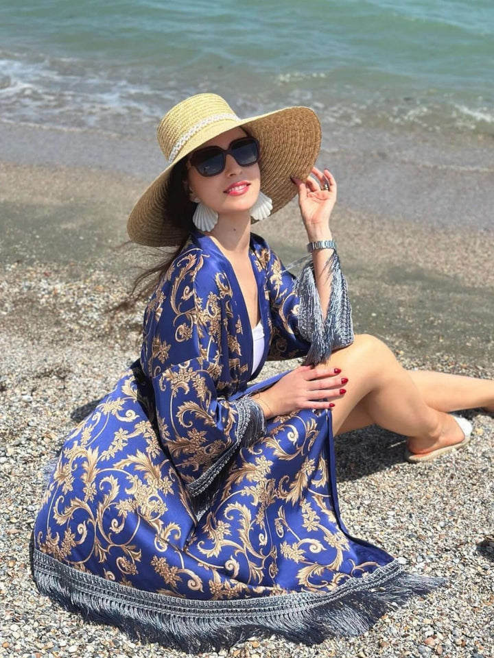 Woman wearing a Tassels Blue Kimono Robe sitting by the beach, accentuated with a sun hat and stylish accessories.