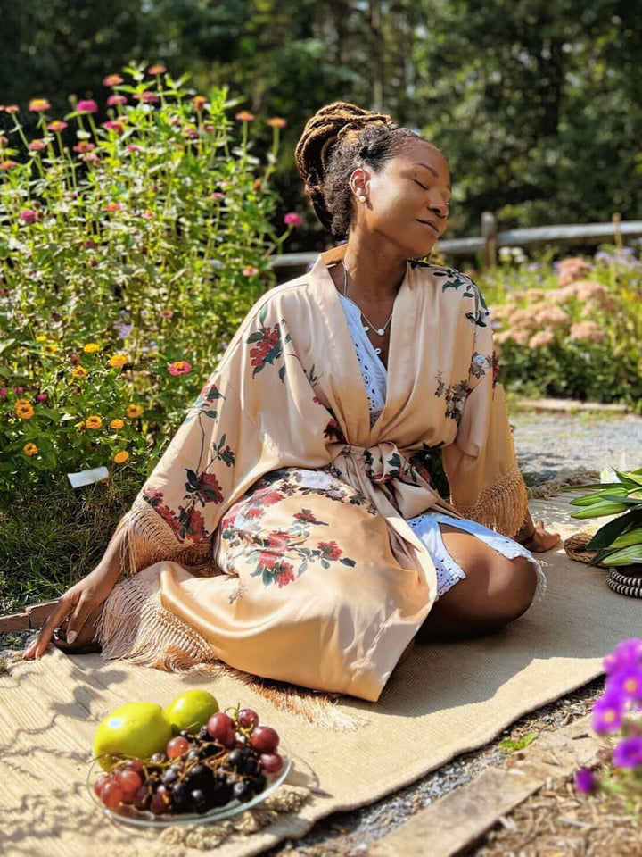 Woman in Tassels Champagne Kimono Robe surrounded by flowers and fruits in a garden setting.