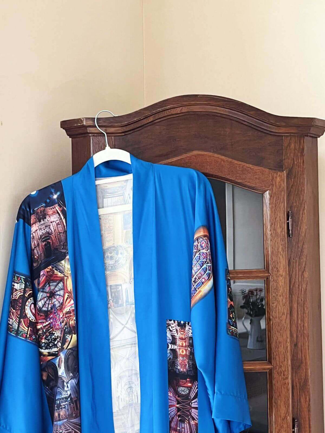 Paris Cathedral Kimono Robe displayed on a hanger against a wooden cabinet, showcasing its vibrant colors and intricate design.