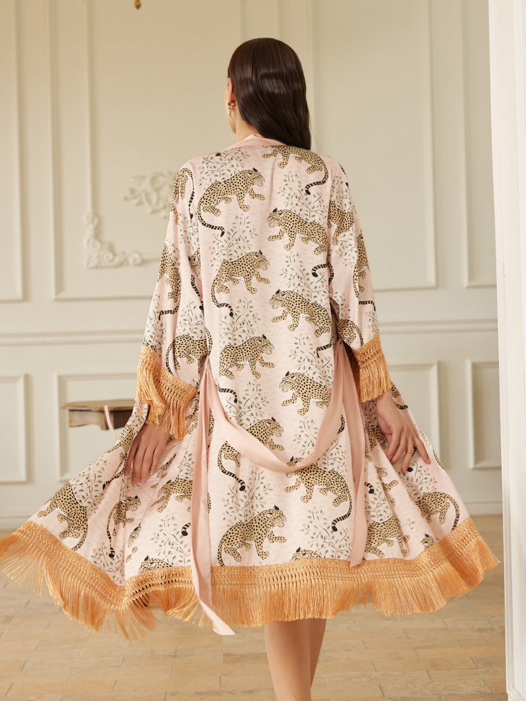 A woman twirls in a Pink Leopard Tassel Kimono Robe showcasing its chic design and luxurious tassels.