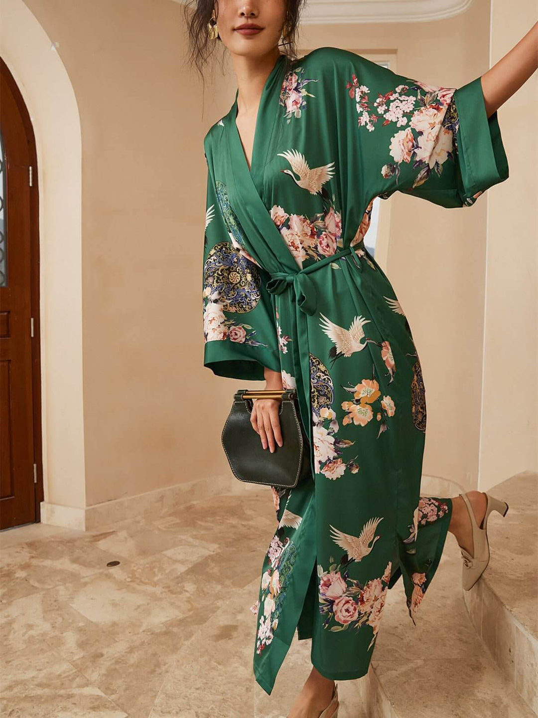 Woman in a Garden Crane Green Kimono Robe, showcasing luxury with floral patterns in a stylish setting.