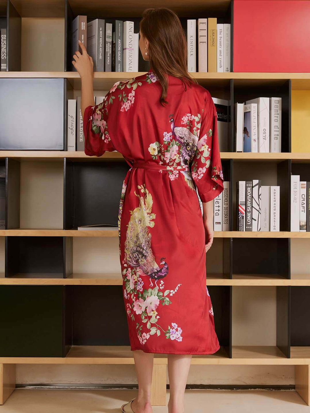 Woman in a Peacock Red Kimono Robe, showcasing luxurious fabric and vibrant floral designs in a modern interior.
