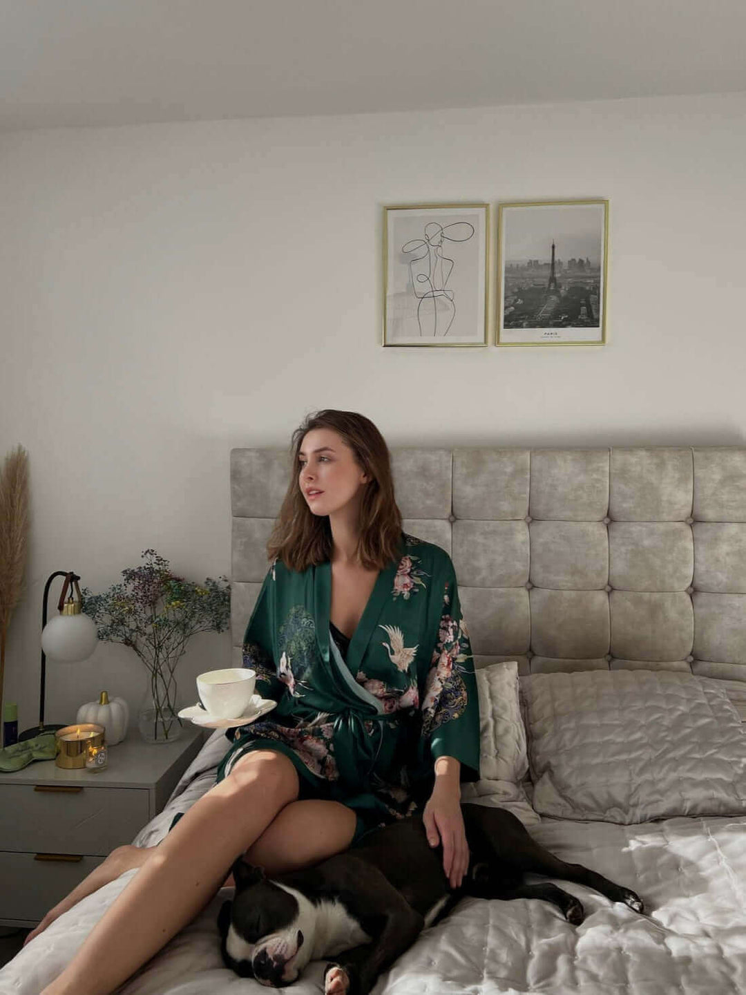 Woman in a Garden Crane Green Kimono Robe sitting on bed, enjoying tea with a dog.