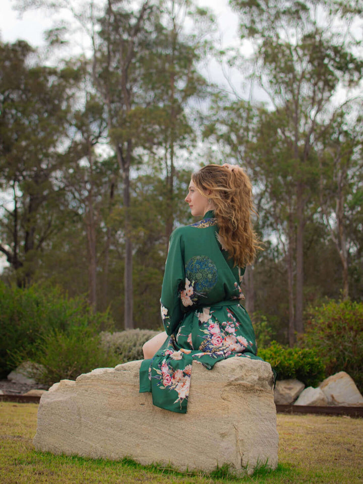 Woman wearing a Garden Crane Green Kimono Robe, showcasing luxury and style in a serene outdoor setting.