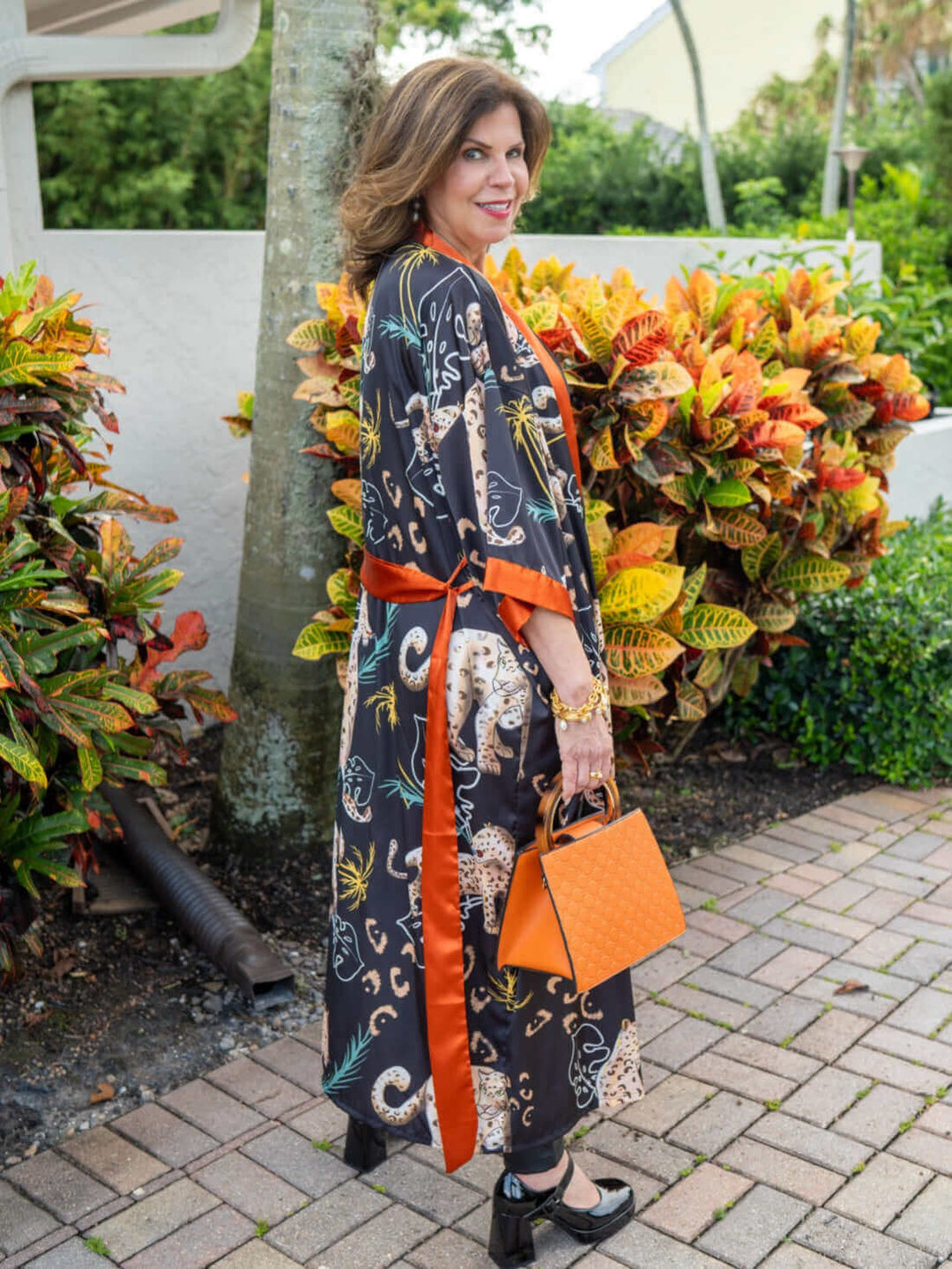 Woman wearing a Jungle Animals Kimono Robe, showcasing vibrant prints and luxurious style in a tropical garden.