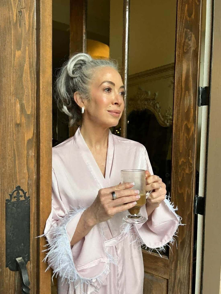 Woman in a pink feather bridal robe holding a drink, showcasing luxury and elegance.