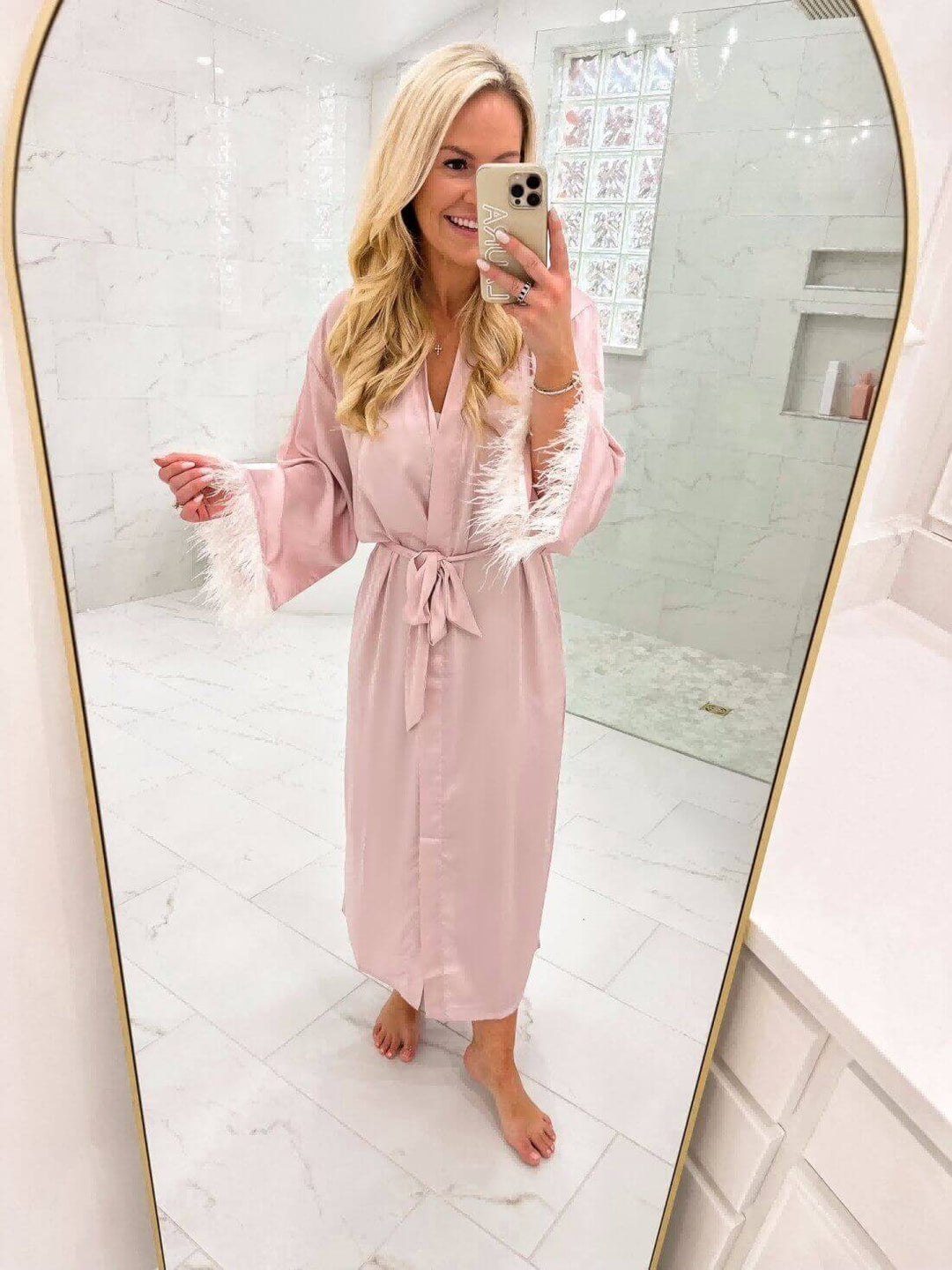 Woman wearing a Pink Feather Bridal Robe in a bright bathroom, showcasing luxury and elegance.