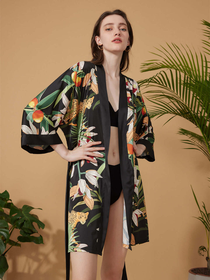Model showcasing Short Kimono Robe Black Leopard against a warm backdrop with tropical foliage.